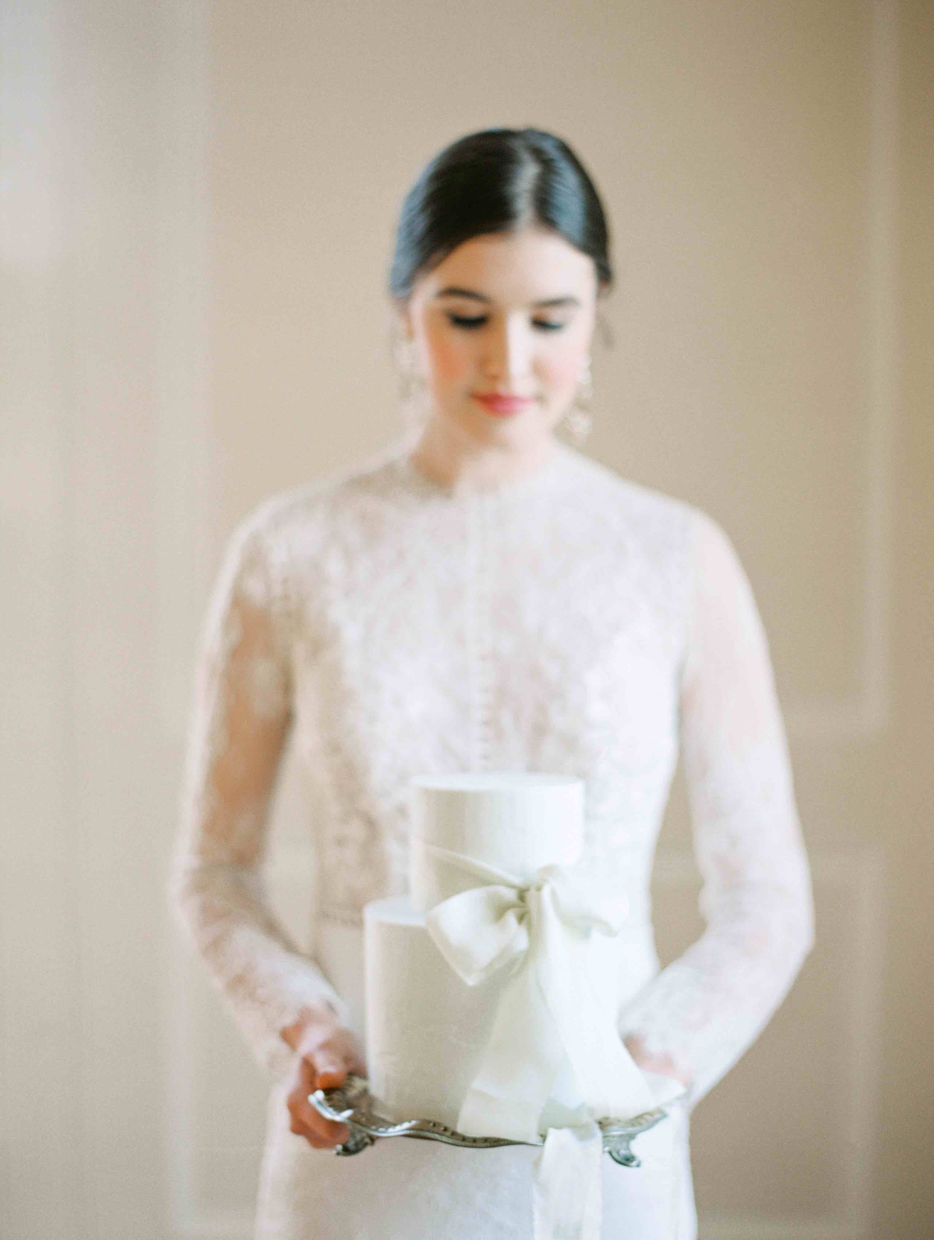 Bride holding elegant buttercream wedding cake tied with a ribbon | The Timeless Stylist | Hannah Duffy