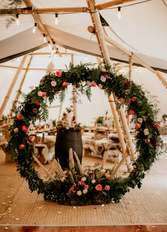 Lots and lots of wildflowers in this floral moongate framing buttercream wedding cake in Surrey tipi wedding. Photo by Elena Popa