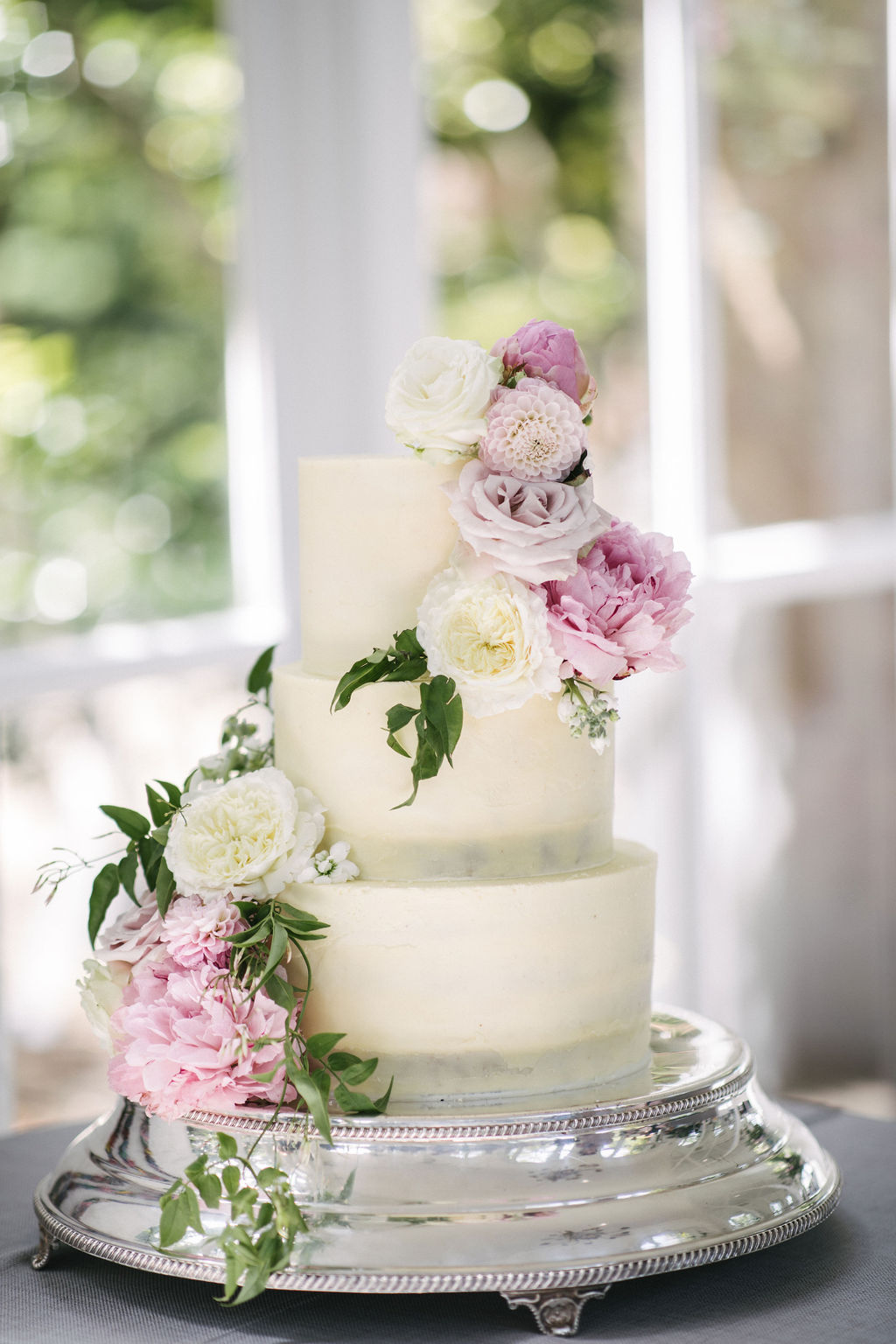 Cascade of fresh flowers in delicate pinks and ivory on this beautiful buttercream wedding cake by Sugar Plum Bakes at The Orangery. Holland Park, London. Photo by Kari Bellamy