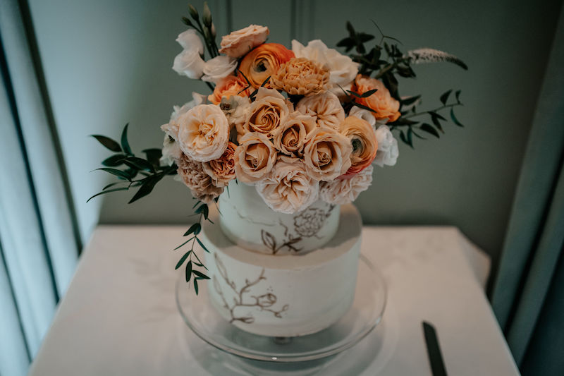 Buttercream wedding cake decorated with hand painted floral detail and explosion of fresh flowers in orange, peach and ivory | Sugar Plum Bakes | Bingham Riverhouse Richmond upon Thames UK | The Unscripted