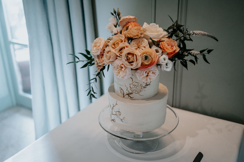 Buttercream wedding cake decorated with explosion of fresh flowers in orange, peach and ivory | Sugar Plum Bakes | Bingham Riverhouse Richmond upon Thames UK | The Unscripted