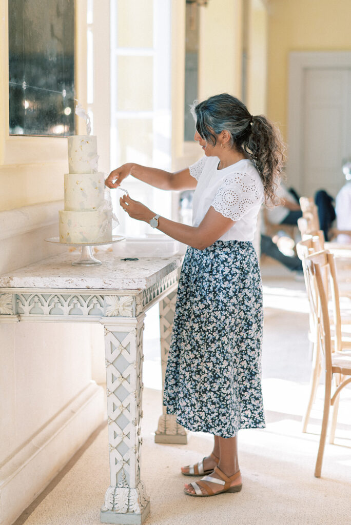 Cake designer at Sugar Plum Bakes adding finishing touches to espoke buttercream wedding cake for Asian bride and groom at Euridge Manor with personalised hand-calligraphed details | Cotswolds