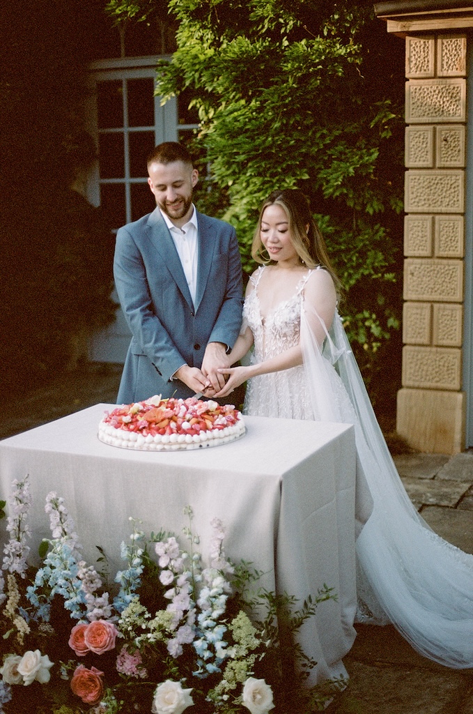 Couple cutting millefoglie wedding cake decorated with fresh fruit and edible flowers at Euridge Manor | The Cotswolds