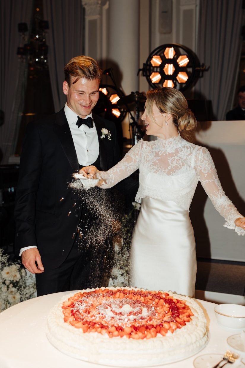 Couple dusting icing sugar on their large Italian pavlova meringue wedding cake | Corinthia London | Lucia Mancini photography