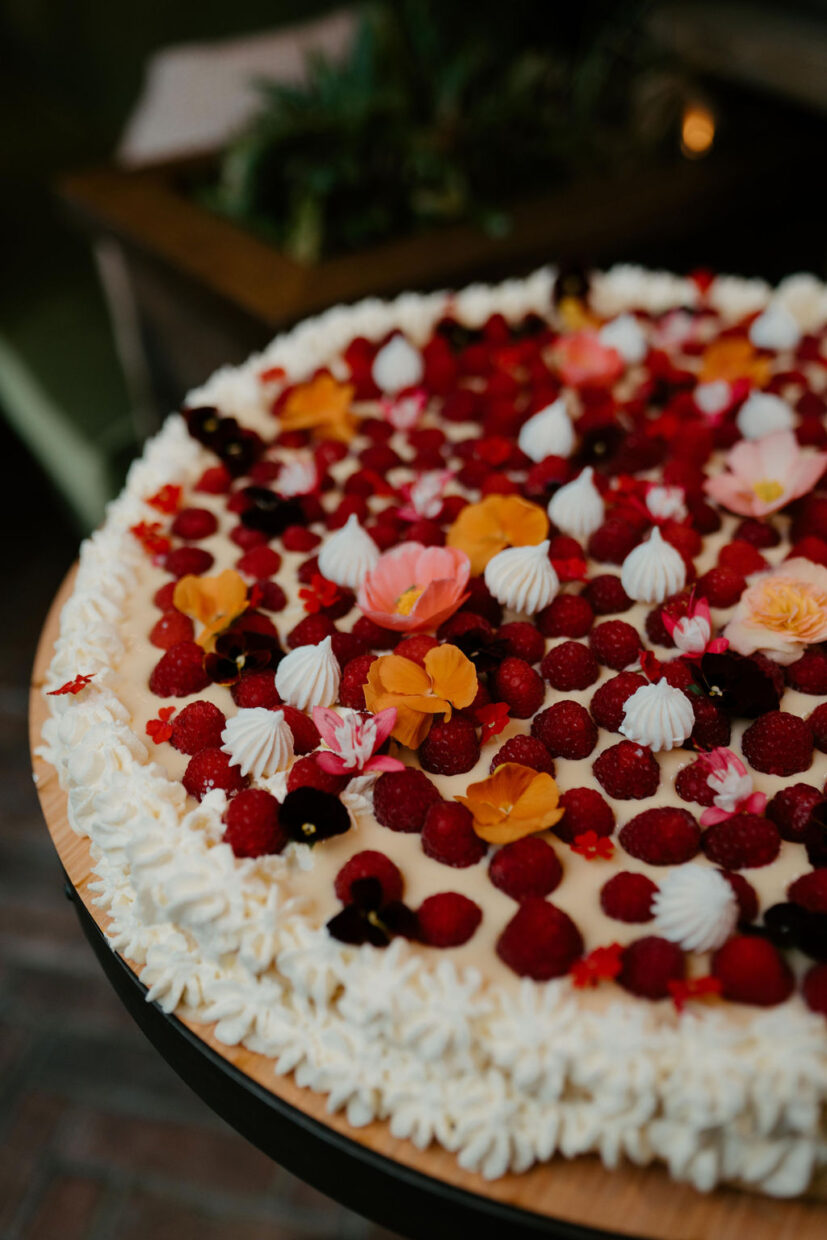 Large Millefoglie Italian wedding cake decorated with fresh raspberries, edible flowers (shades of red and orange) and meringue kisses